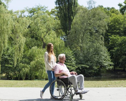 Young girl walking in the park with elder man on a wheelchair